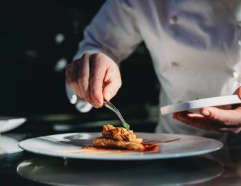 A chef is finishing the preparation of the plate. He's decorating the plate just before the serving.