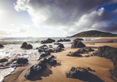 Pristine beach in Hawaii with large volcanic stones on shore