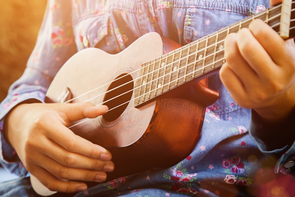 Close-up of little hipster girl playing ukulele guitar, vintage film tone effect