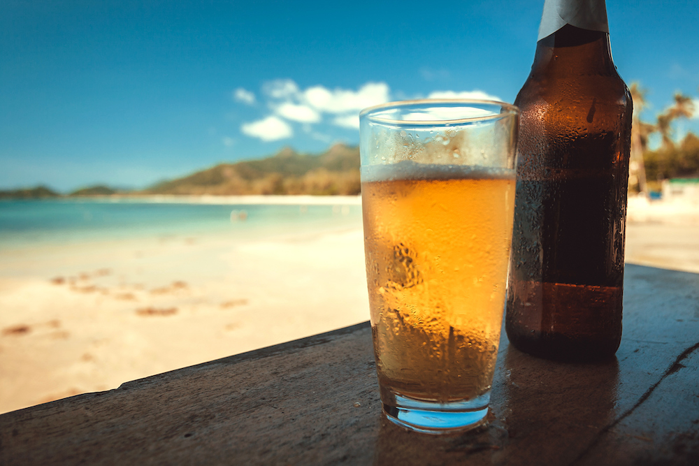 beer bottle and a glass of beer on a table at a beach location