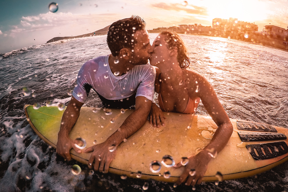 couple kissing while holding onto a surfboard in the ocean